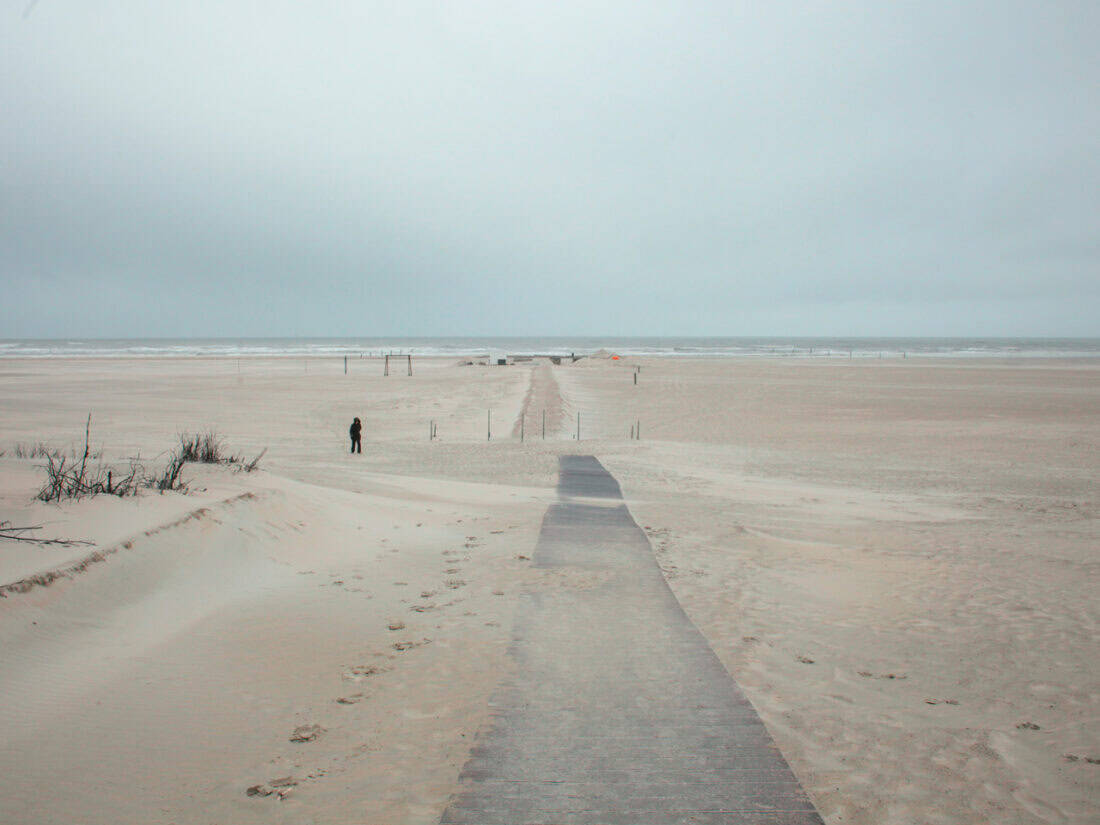 Frau im Parka kämpft mit dem Wind am einsamen Strand von Norderney