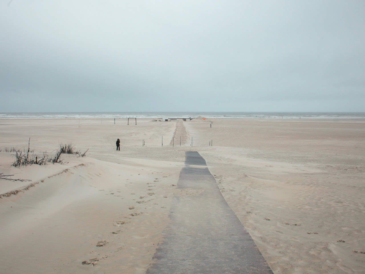 Frau im Parka kämpft mit dem Wind am einsamen Strand von Norderney