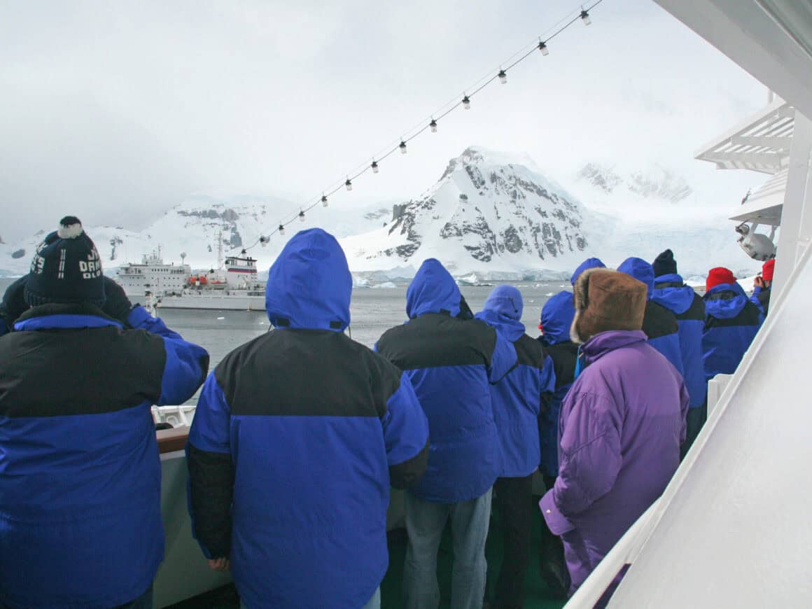 Touristen auf Kreuzfahrtschiff in der Antarktis blicken auf Gletscher und weitere Kreuzfahrtschiffe im Eis