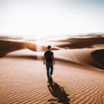 Ein Mann steht alleine in der Wüste Dubais und schaut in den Horizont, den Rücken zur Kamera gewandt.