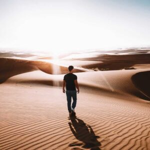Ein Mann steht alleine in der Wüste Dubais und schaut in den Horizont, den Rücken zur Kamera gewandt.