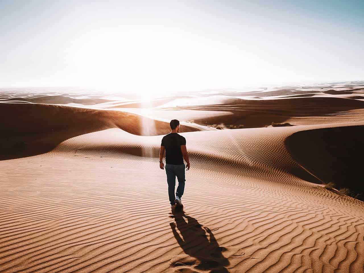 Ein Mann steht alleine in der Wüste Dubais und schaut in den Horizont, den Rücken zur Kamera gewandt.