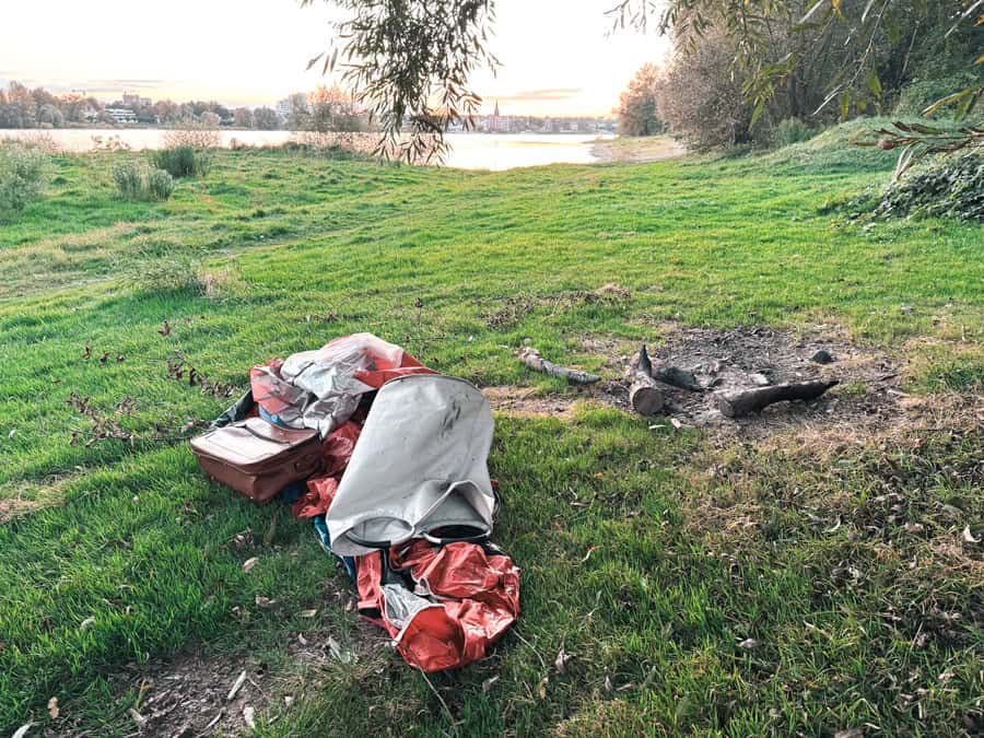 Zurückgelassenes Zelt und Outdoor-Equipment mit Lagerfeuer am Rhein