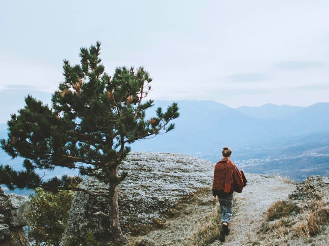 Nachdenkliche Frau steht in einer weiten Landschaft und blickt nach unten, symbolisiert die inneren Zweifel und Fragen beim Auswandern in ein anderes Land.