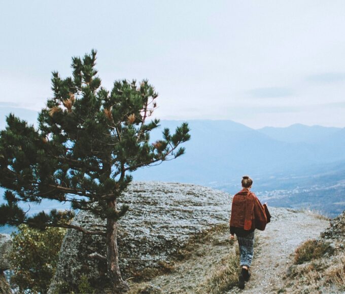 Nachdenkliche Frau steht in einer weiten Landschaft und blickt nach unten, symbolisiert die inneren Zweifel und Fragen beim Auswandern in ein anderes Land.