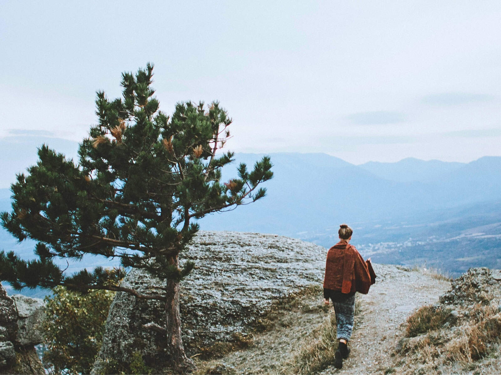 Nachdenkliche Frau steht in einer weiten Landschaft und blickt nach unten, symbolisiert die inneren Zweifel und Fragen beim Auswandern in ein anderes Land.