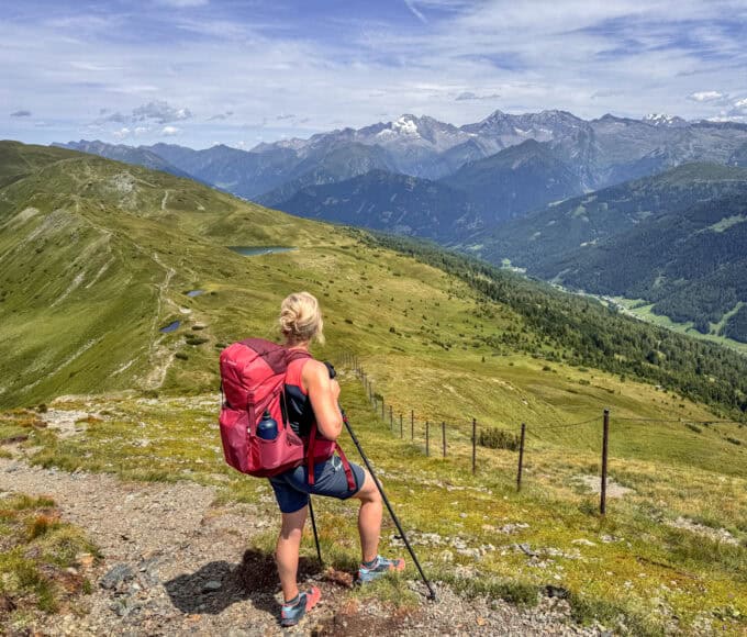 Wanderin mit rotem Rucksack auf einem Höhenweg in den Alpen mit Blick auf Berge und Tal während einer Eurohike-Wanderreise von Innsbruck nach Sterzing.