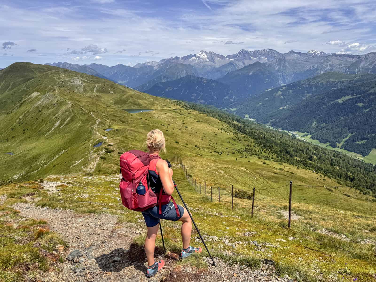 Wanderin mit rotem Rucksack auf einem Höhenweg in den Alpen mit Blick auf Berge und Tal während einer Eurohike-Wanderreise von Innsbruck nach Sterzing.
