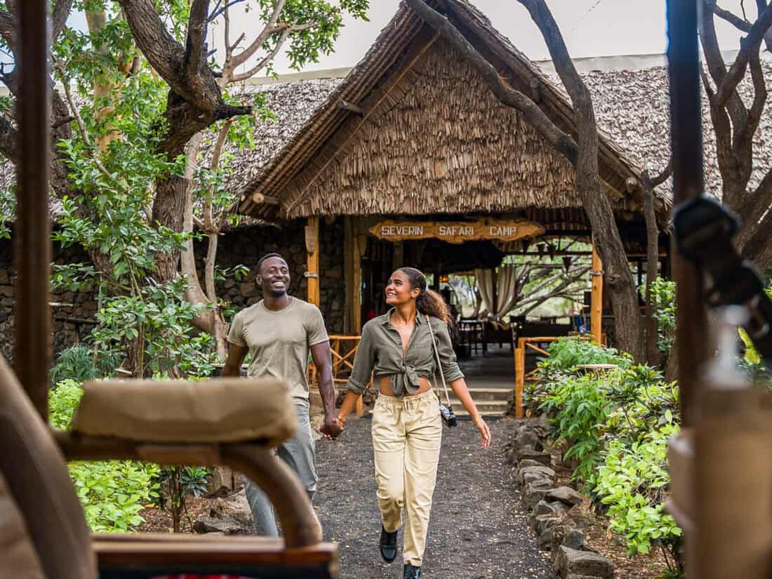Zwei Reisende gehen vor dem Severin Safari Camp in Kenia durch eine grüne Lodge-Anlage.