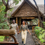 Zwei Reisende gehen vor dem Severin Safari Camp in Kenia durch eine grüne Lodge-Anlage.