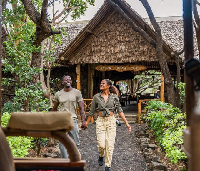 Zwei Reisende gehen vor dem Severin Safari Camp in Kenia durch eine grüne Lodge-Anlage.