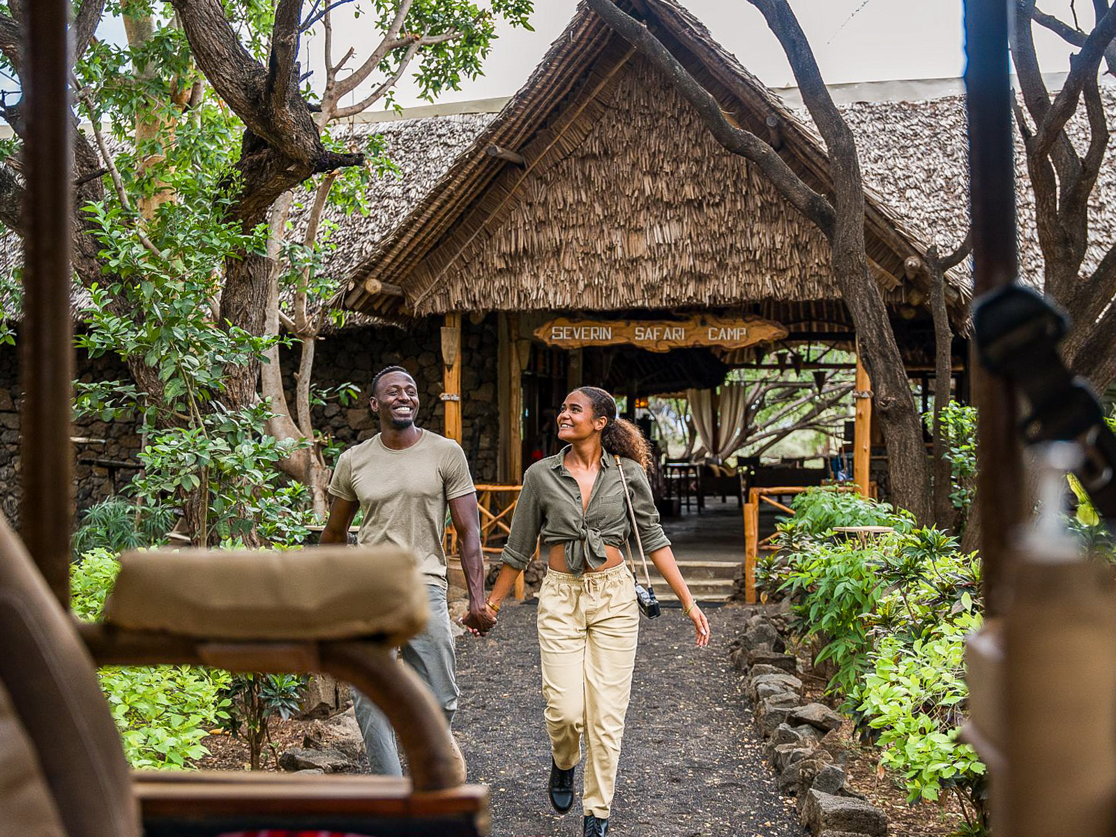Zwei Reisende gehen vor dem Severin Safari Camp in Kenia durch eine grüne Lodge-Anlage.