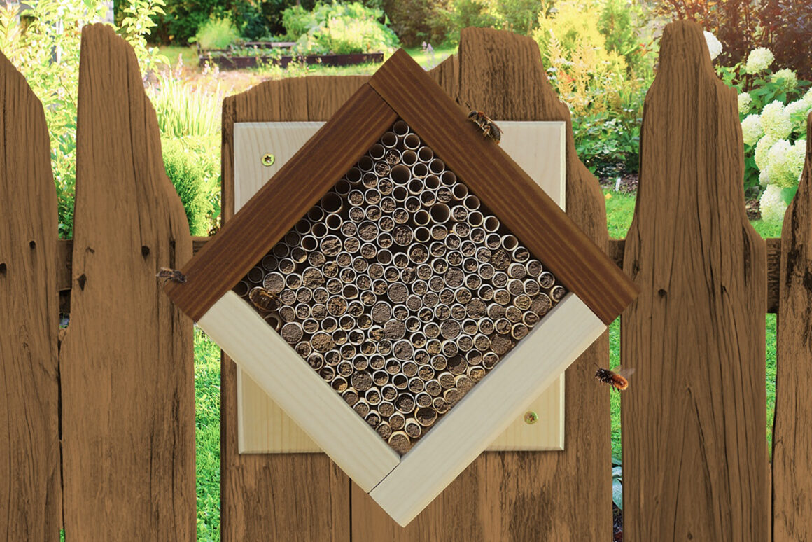 Wildbienenhaus mit zahlreichen Niströhren an einem Holzzaun in einem naturnahen Garten.